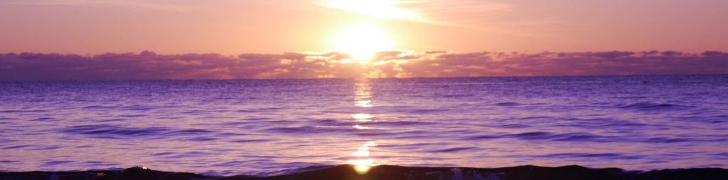 Beach front sunset, the water appears purple due to the shade of the sunset.